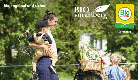 Auschnitt des Titelblatts vom Bio-Einkaufsführers Vorarlberg 2024 - Frau mit gefülltem Einkaufskorb am Fahrrad und 2 Kindern.