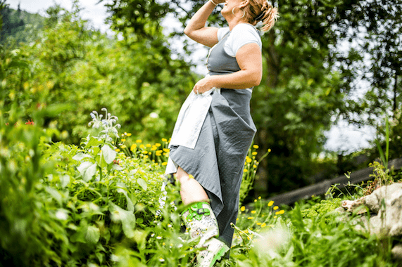 Biobäuerin steht im Hausgarten und blickt in den Himmel.